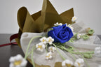 Handmade crochet flower bouquet featuring a single blue rose with baby's breath and greenery, wrapped in brown paper and laid on a dark table.
